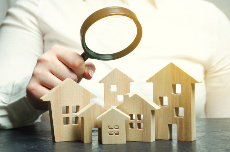 A woman is holding a magnifying glass over a wooden houses. Real estate appraiser. Property valuation / appraisal. Find a house. Search for housing. Real estate market analysis. Selective focus